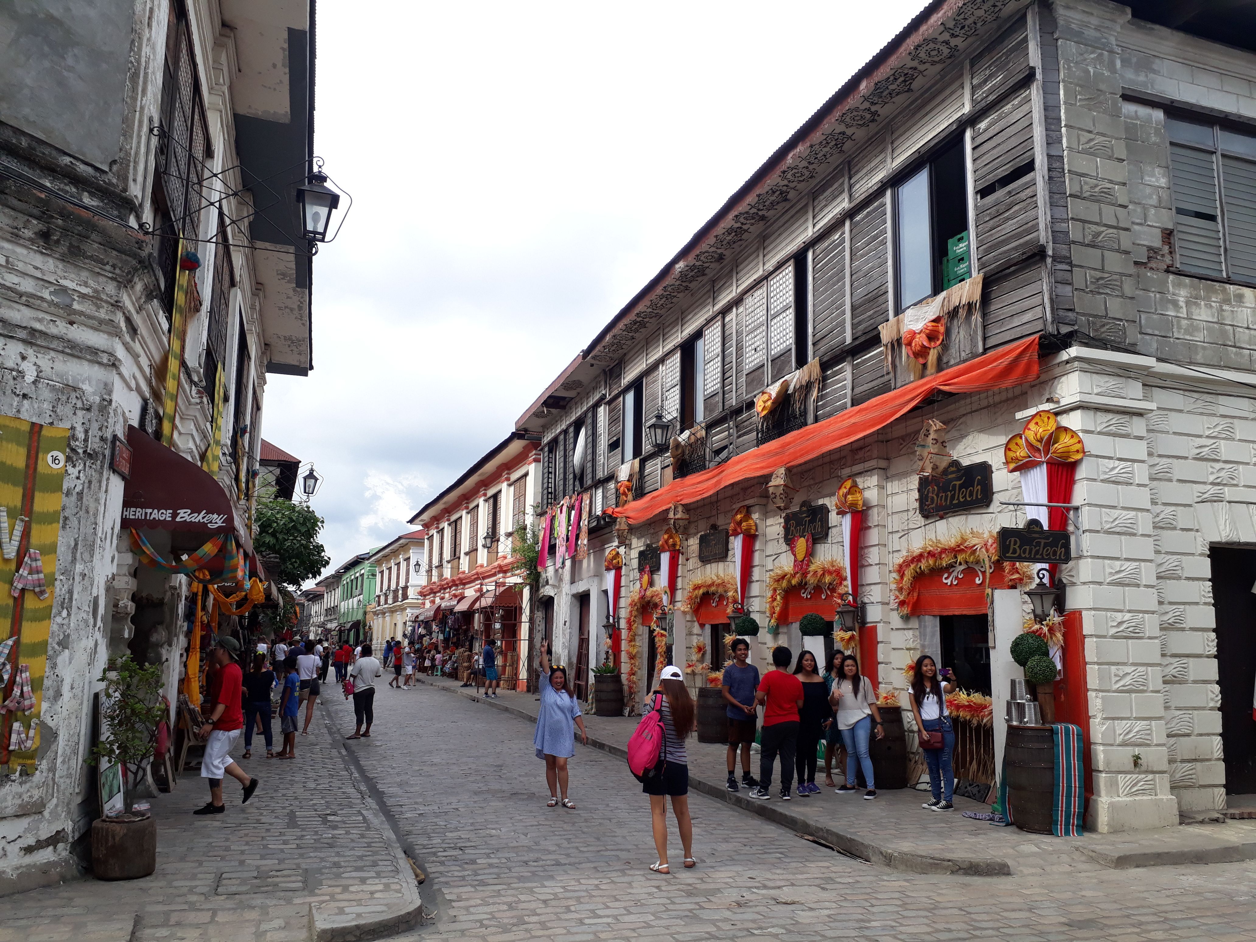 Visitors walking along Calle Crisologo between rows of historic houses and shops.