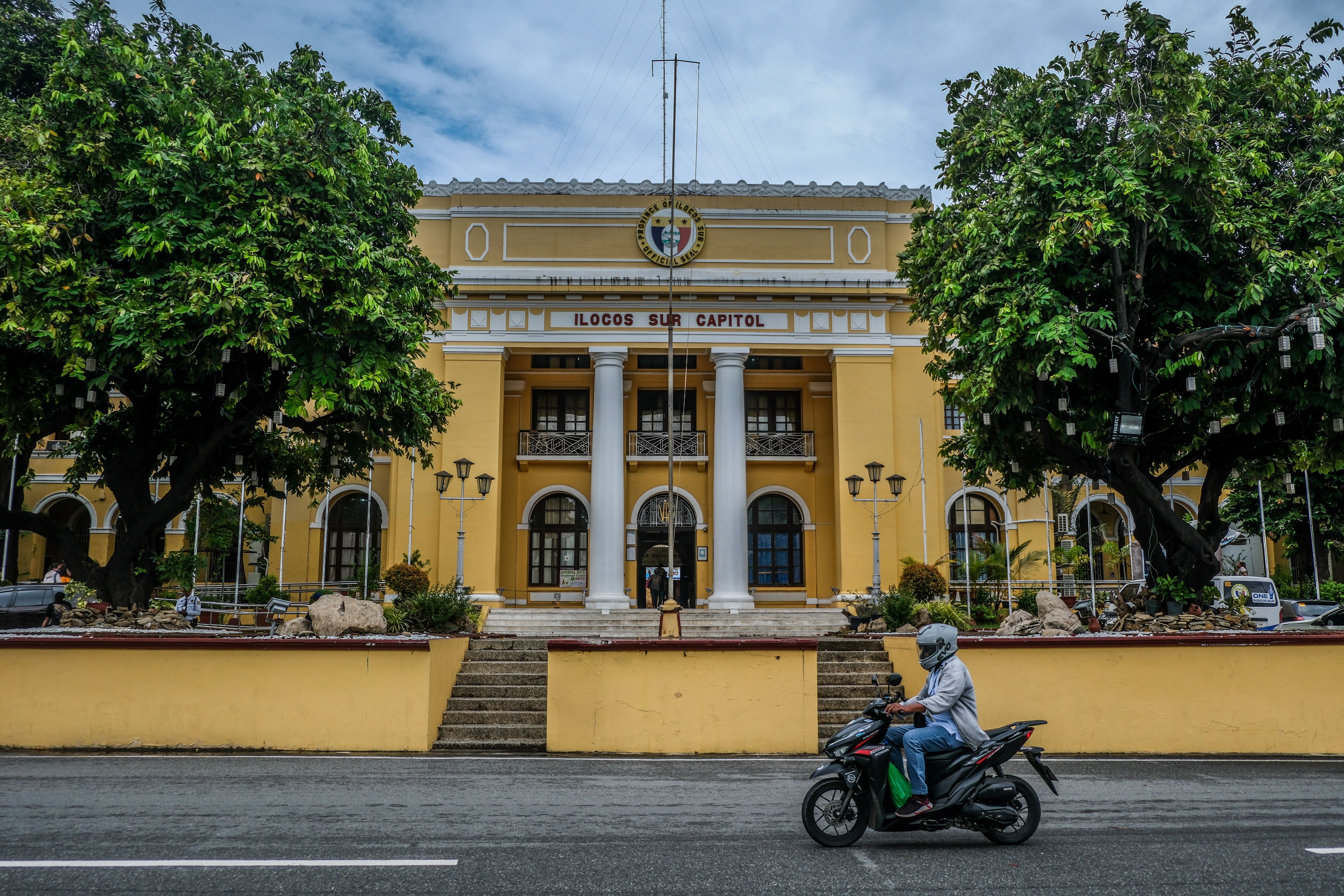 The ochre façade and columned entrance of the Ilocos Sur Provincial Capitol, framed by trees.